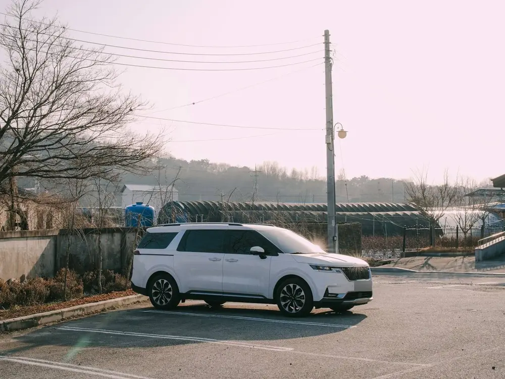 White Kia Carnival parked under an open sky