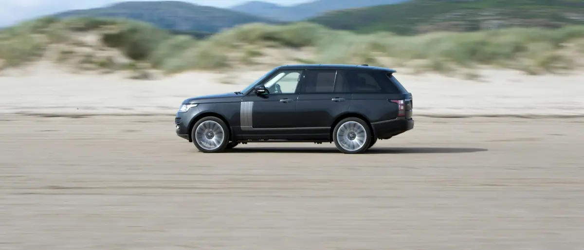 Range Rover on a coastal road with hills behind